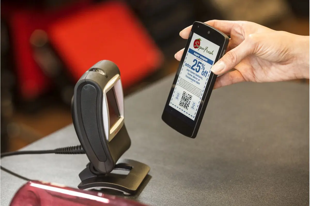 Hand hält Smartphone mit QR-Coupon vor Barcode-Scanner